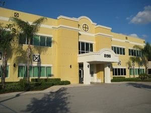 A large yellow building with palm trees in front of it.